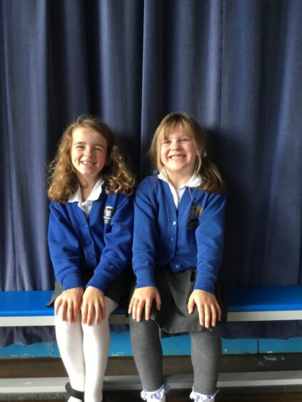 Lumphanan School's two P1 pupils sitting on a bench with a curtain behind them