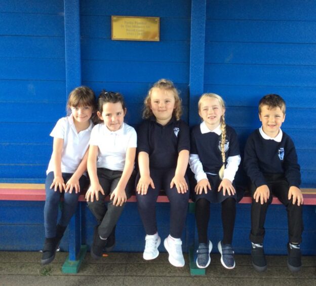Lybster Primary School's primary one, five pupils sitting on a bench with a bright blue wall behind them