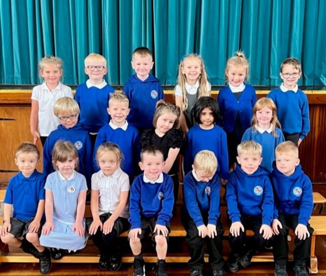 Mrs Mackenzie's class at Macduff Primary split into three rows with the assembly hall stage behind them