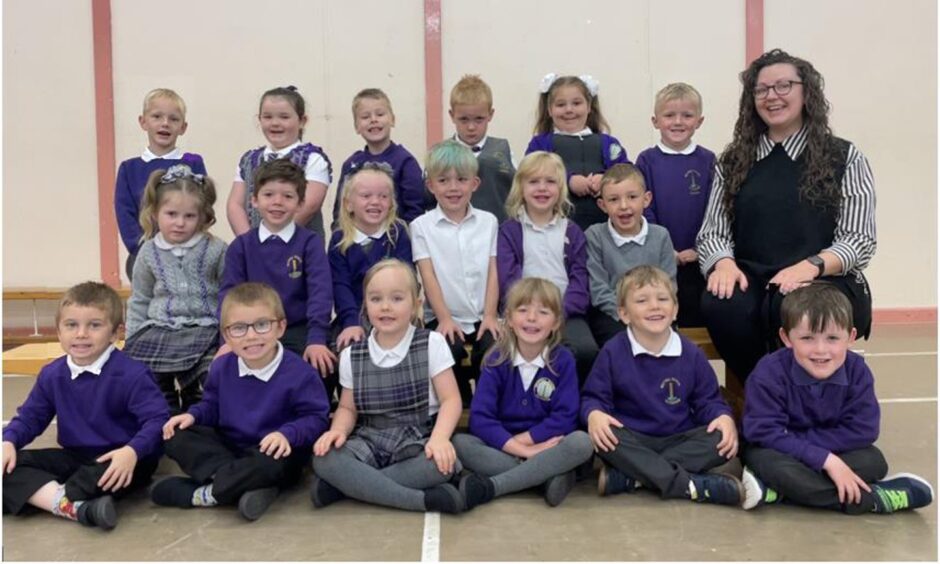 Meethill Primary School's P1 class in three rows with their teacher sitting on the bench beside them