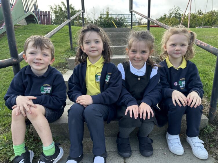 Four P1 pupils from Midmar Primary School, sitting on a set of stairs in the playground.