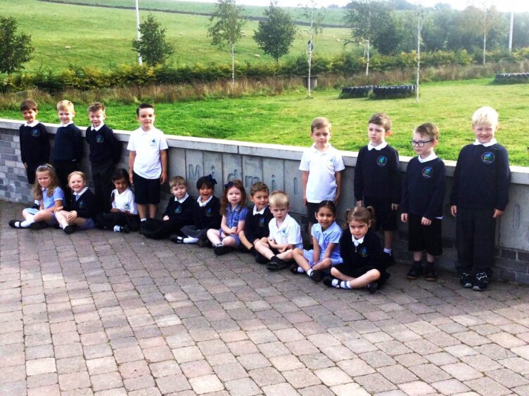 Pupils at Midmill School, sitting and standing against a concrete wall with the schools name engraved in it.