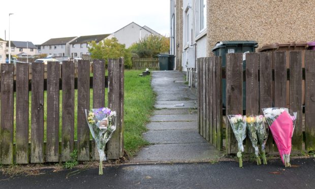 Flowers propped up at wooden gate on Anderson Drive with pathway behind.