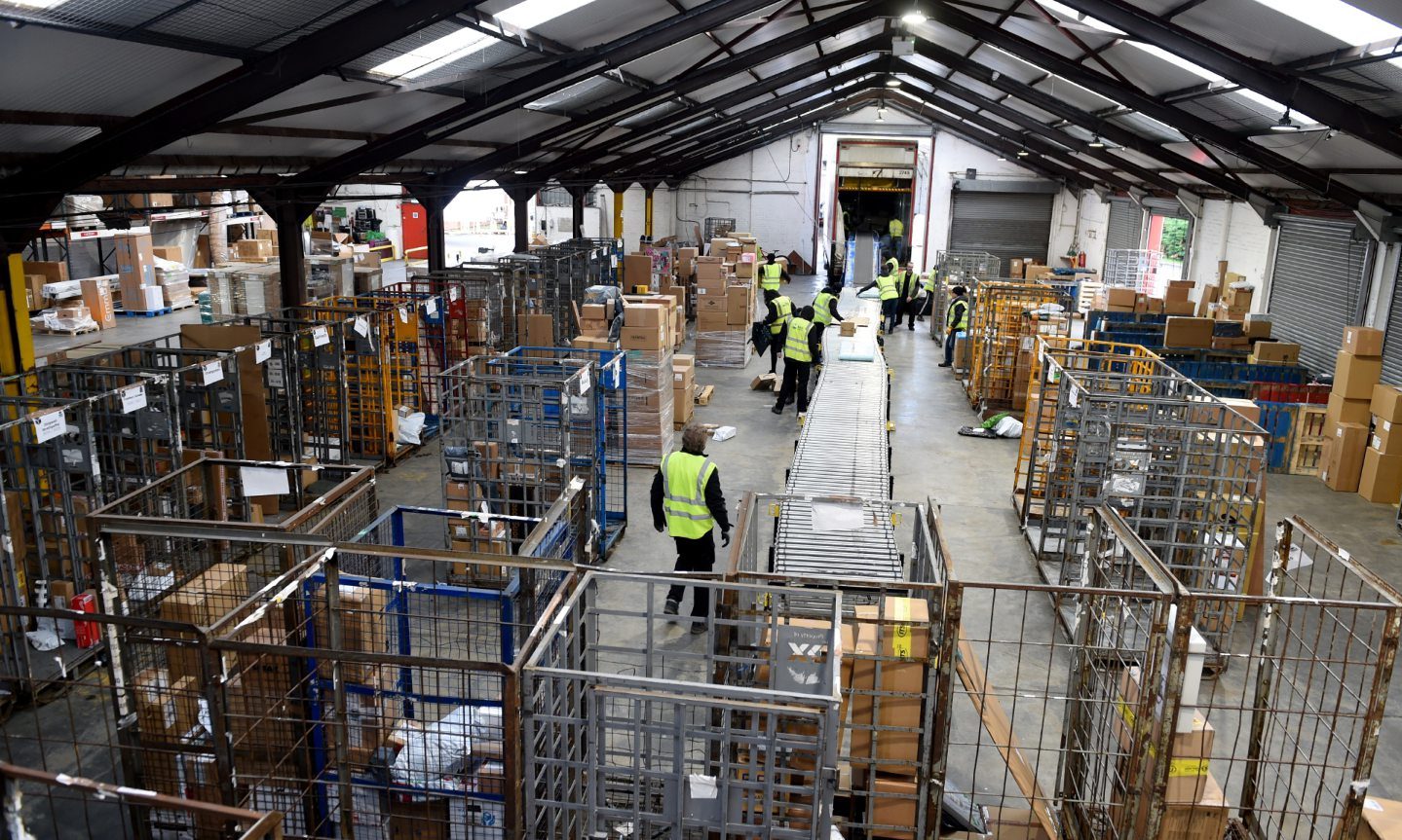 Wide view of warehouse with conveyor belt, parcels and cages. 