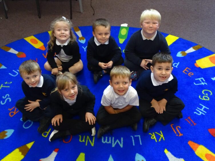 First class of 2023 at Portknockie Primary School in Moray, with seven pupils sitting with their legs crossed on a colourful round rug with the alphabet on it 
