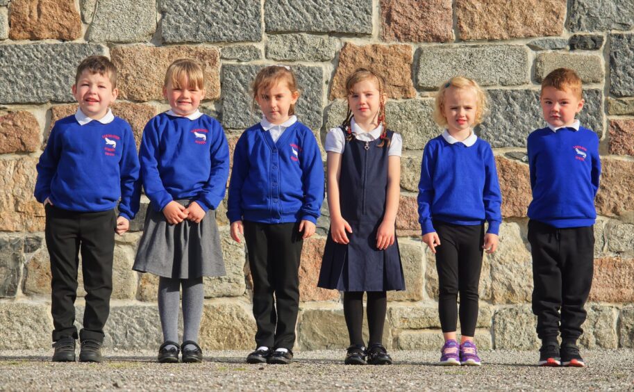 Six Sandhaven School primary 1 pupils lined up with a stone wall of the school building behind them