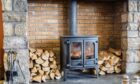Shutterstock image of a wood burning stove in a brick fireplace with a pile of wood next to it.