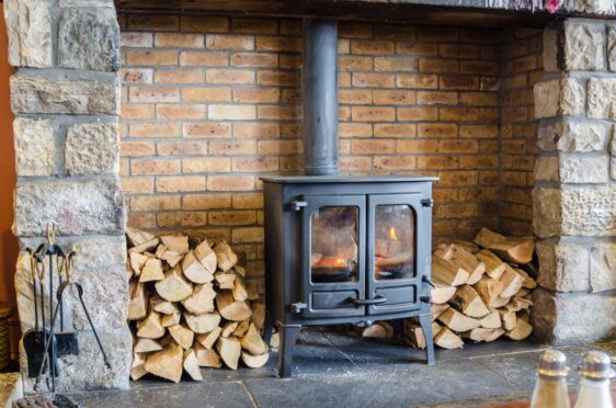 Shutterstock image of a wood burning stove in a brick fireplace with a pile of wood next to it.