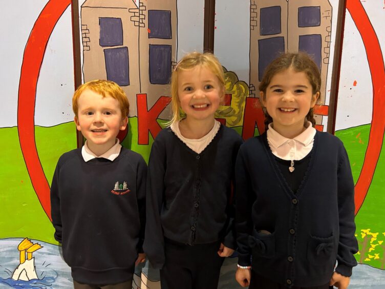 Three Skene School pupils, a colourful mural on the wall behind them