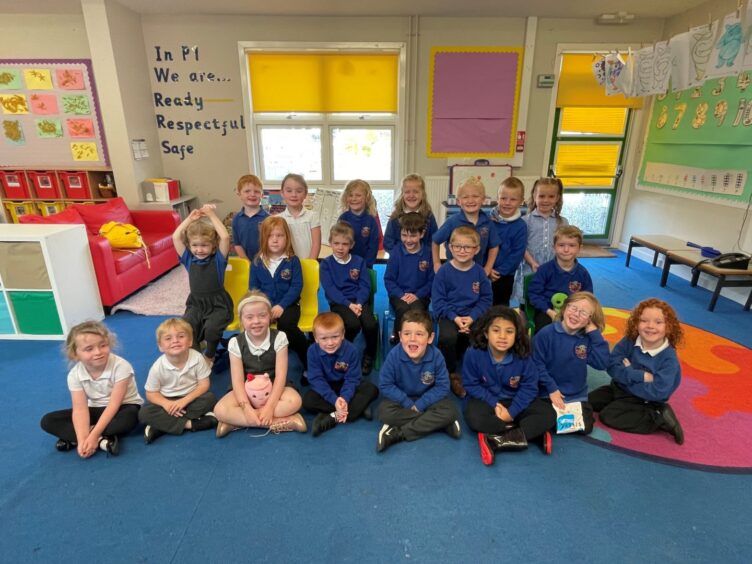 Smithton Primary School's class P1GO in a colourful classroom with the words 'In P1 we are... ready - respectful - safe'. The children are in three rows and smiling at the camera