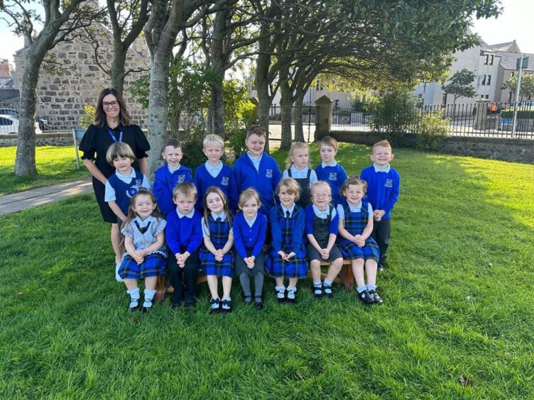 Class P1H at St Andrews Primary sitting in two rows outside the school with their teacher standing next to them
