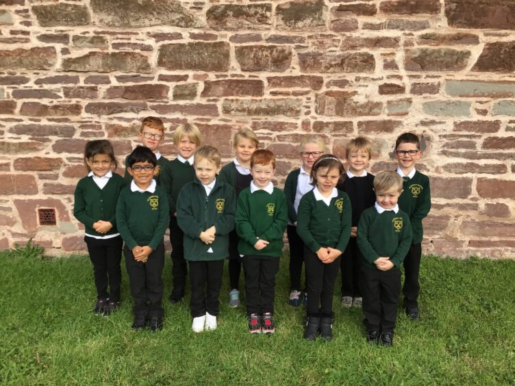 First Class of 2023 at Moray school St Peter's Primary School in Buckie. The children are in two rows on the grass outside the school with a cobbled brick wall behind them