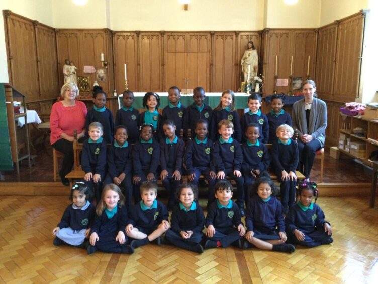 Class P1HS at St. Joseph's RC Primary School sitting/standing in three rows with two staff members 