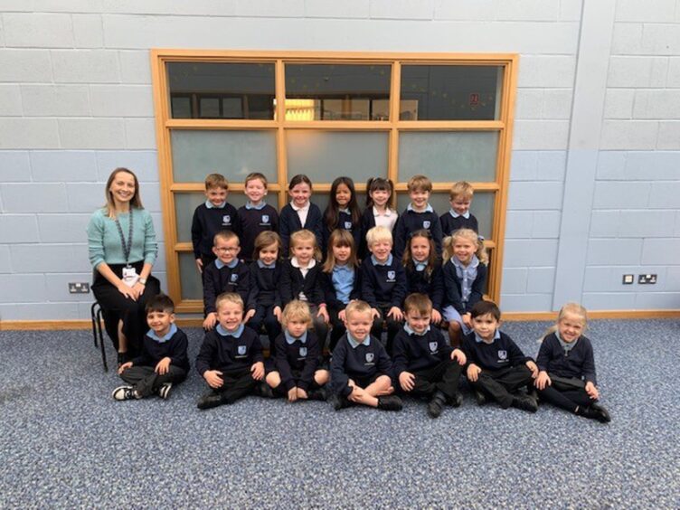 Class P1S at Strathburn School, the First Class of 2023 at the Aberdeenshire school. Their teacher is sitting on a chair next to the three rows of pupils.