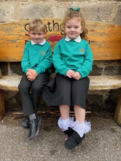 First class of 2023 at Strathgarve Primary School in the highlands and islands - two children sitting on a wooden bench outside the school