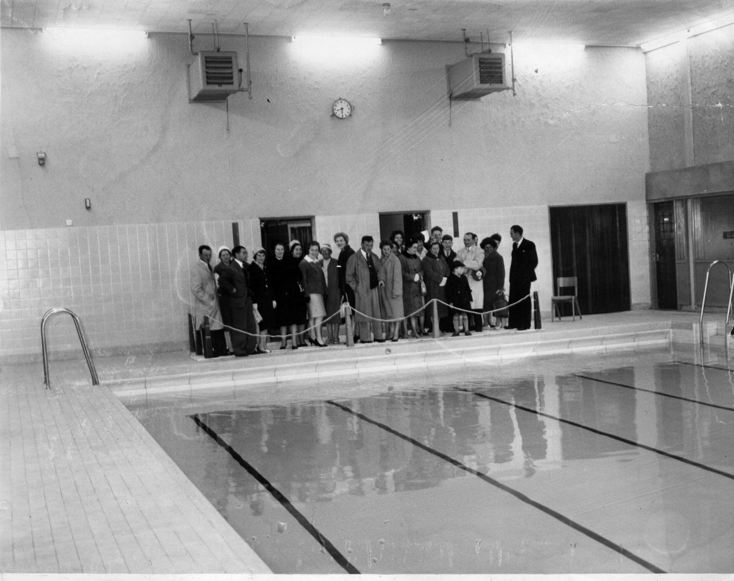 A small group of parents stand behind a cordon at the side of a large swimming pool at the opening of Summerhill Academy in 1962.