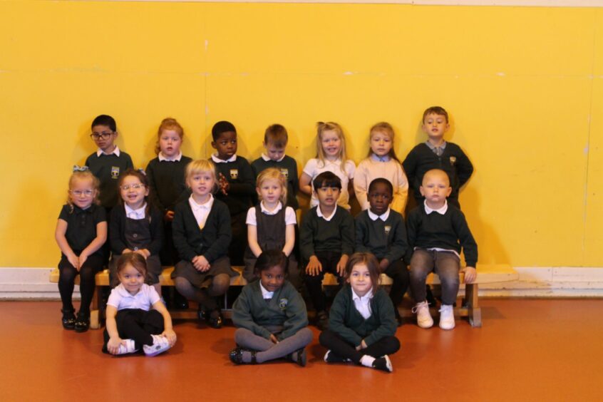Class P1C at Sunnybank Primary School in front of a bright yellow wall.