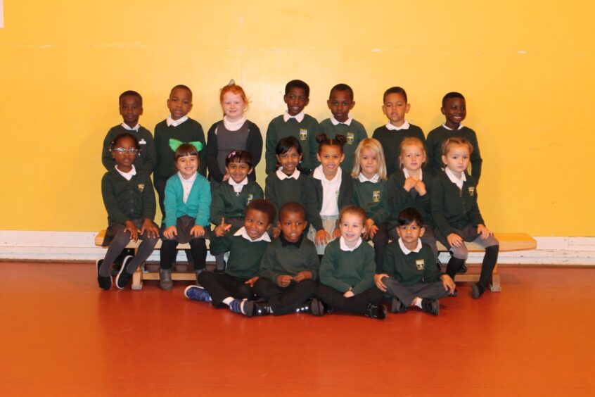 Class P1R at Sunnybank Primary School in three row in front of a bright yellow wall