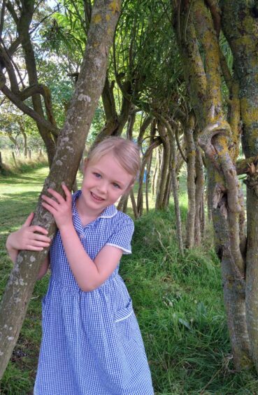 A single primary 1 girl at Tipperty Primary School, pictured with her arm around a tree