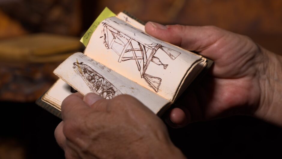 Hands hold a tiny notebook filled with sketches for woodworking projects of Tim Stead