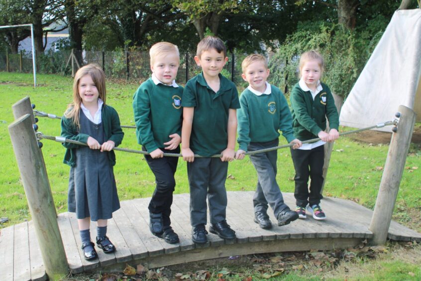 Five primary 1 pupils standing on an small wooden arched bridge in the Udny Green School playground. They are the First class of 2023 at the Aberdeenshire school