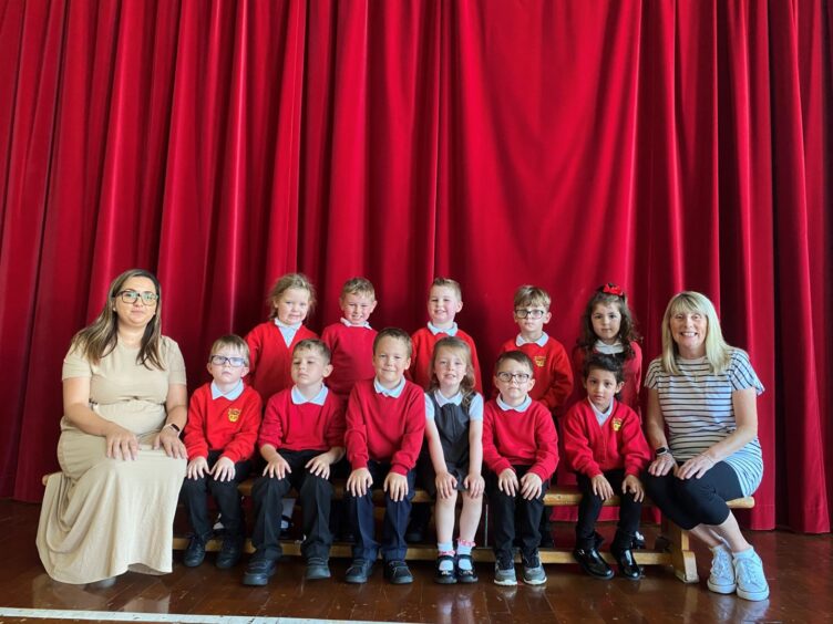 Class P1V at Westpark School in front of a large red curtain with two teachers