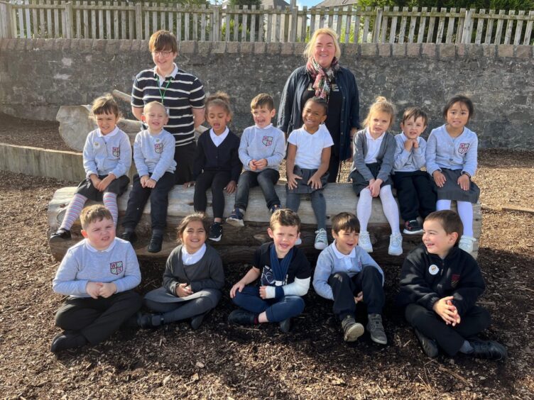 Class P1B at Woodside Primary sitting in two short rows, with members of staff behind them