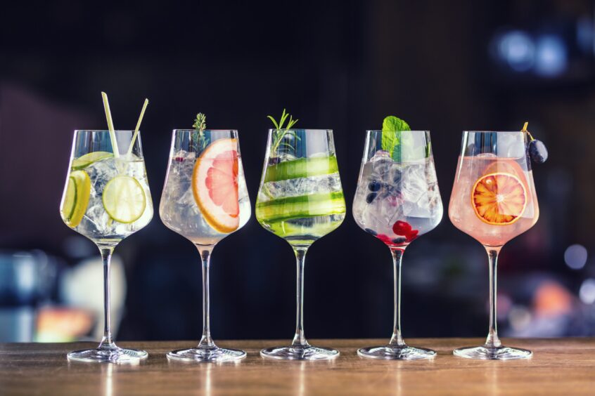 Five colorful gin tonic cocktails in wine glasses on bar counter.