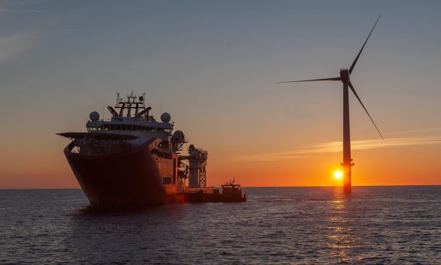 Service operational vessel, with crew transfer vessel alongside and sun setting on wind turbine.