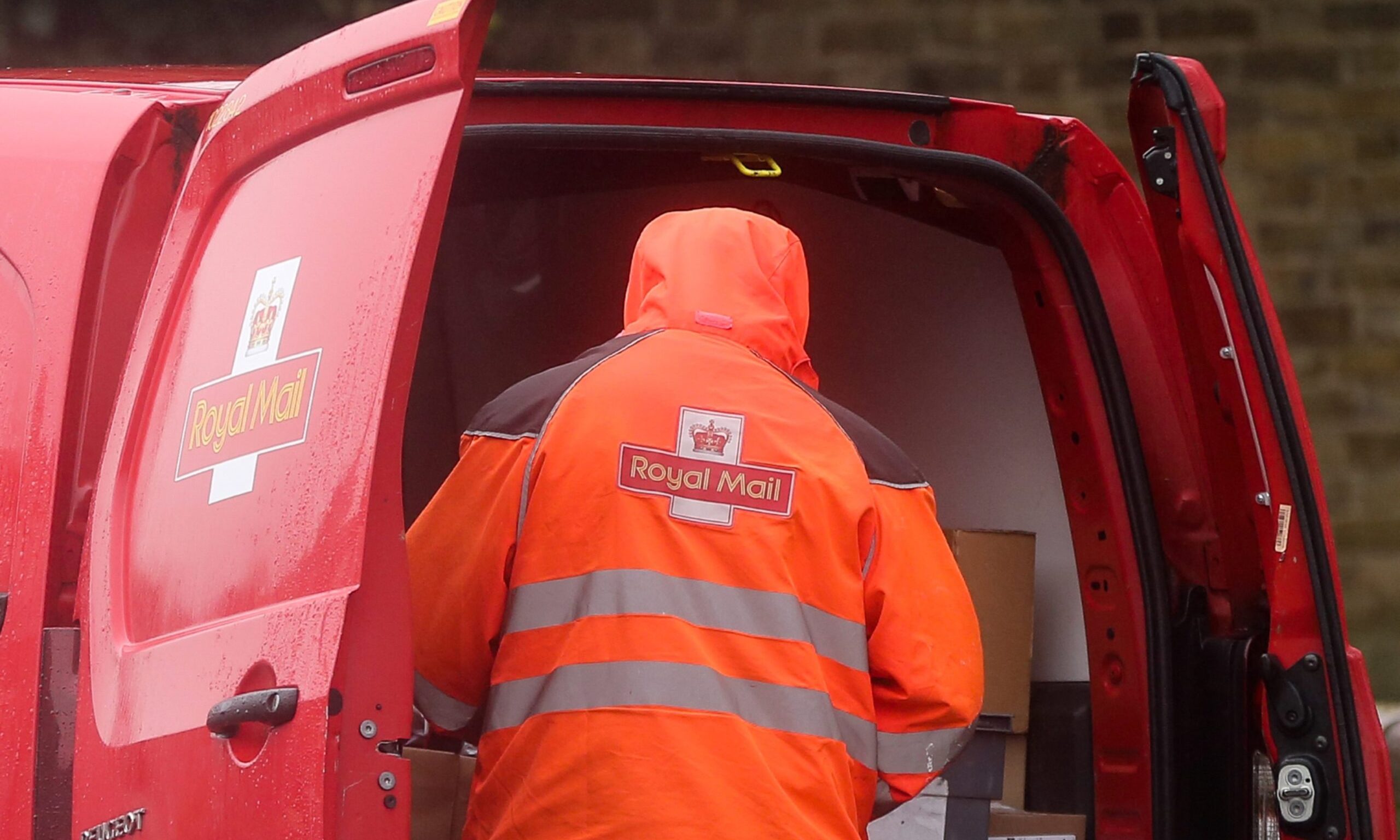 Royal Mail worker from behind looking into post van. 