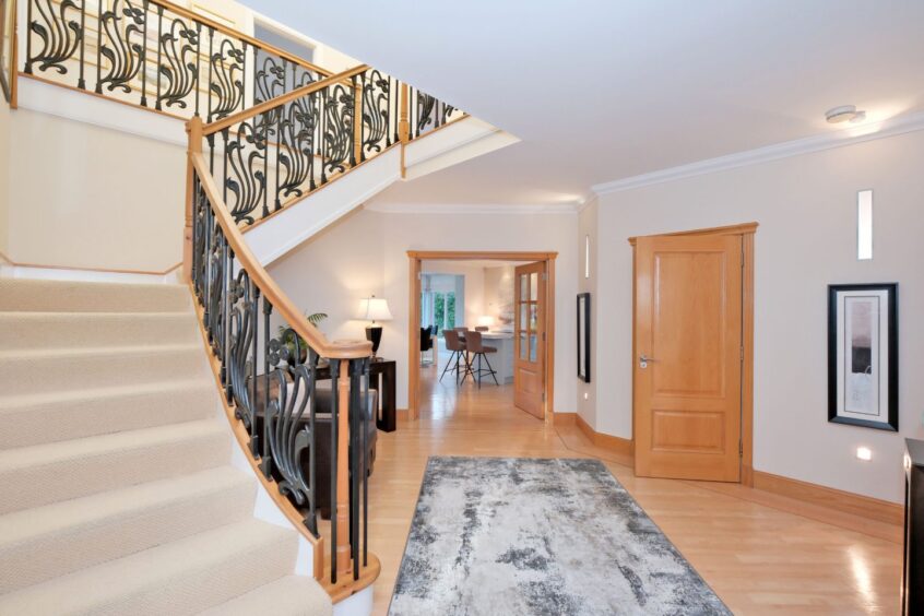 The hallway in the home, with a staircase with an intricate designed bannister and double doors leading to the kitchen