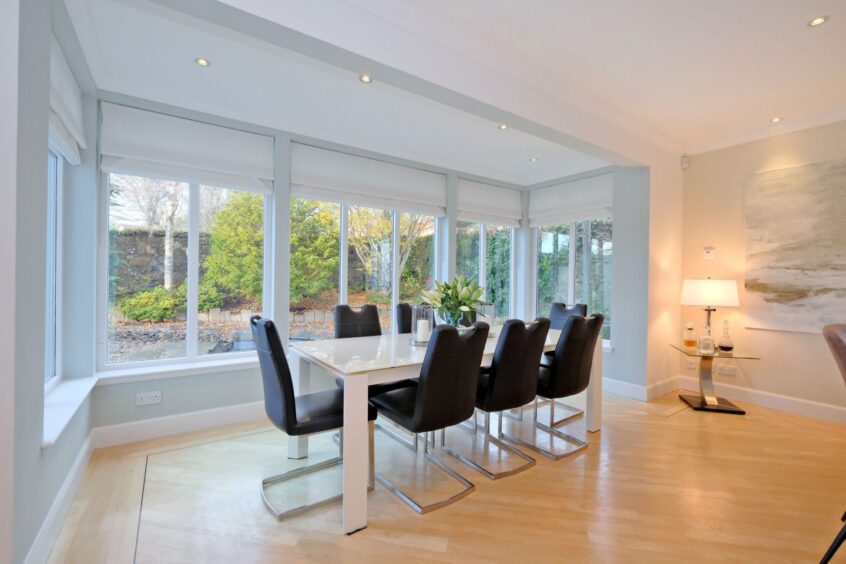 The dining room with 8 black dining chairs and a long white table. There are lots of windows, letting in plenty of natural light