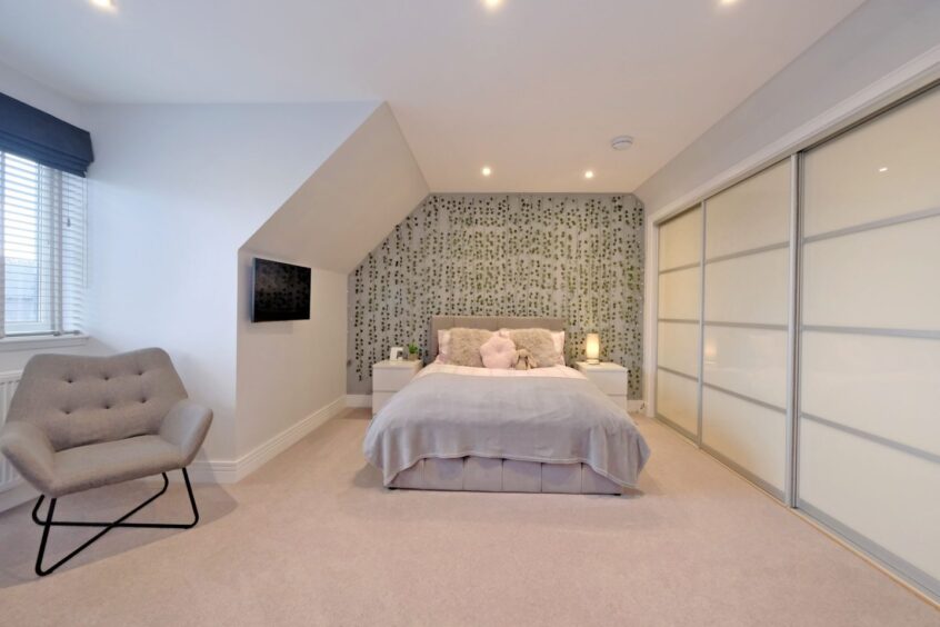 A bedroom in the modern home near Newburgh, with white walls, a cream carpet, built in wardrobe, armchair and cosy double bed