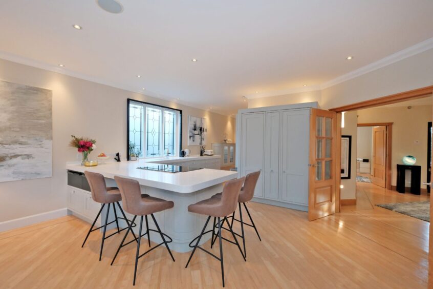 The kitchen in the five-bedroom house Bieldside with a breakfast bar, four modern bar chairs and pantry cupboards.