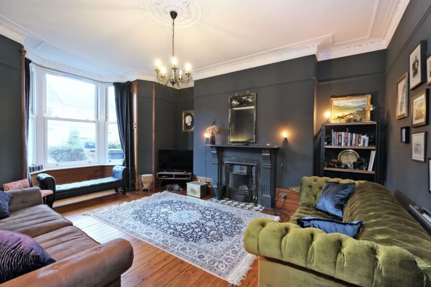 The living room in the Aberdeen renovated home. There are three couches, dark painted walls, wooden floors, a bookcase and a fireplace