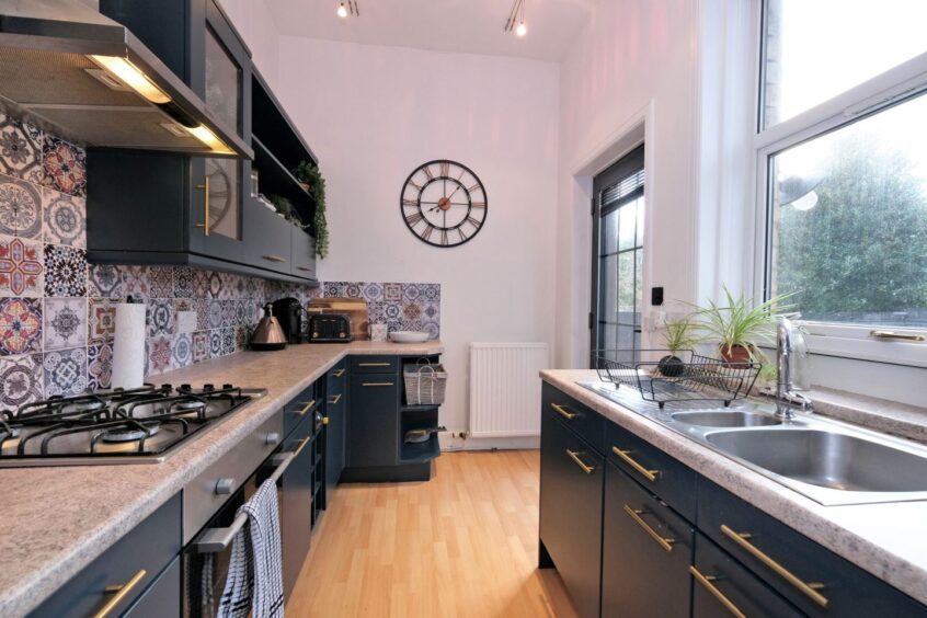 The kitchen with sleek dark cupboards, grey marbled countertops and a patchwork tile backsplash