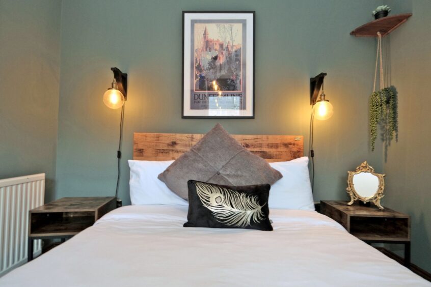 The bedroom has a double bed, two rustic lamps hanging on either side of the bed, a wallmounted print above the headboard and two bedside tables