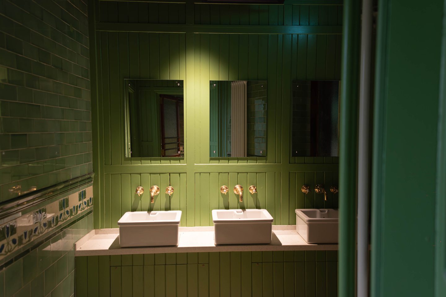 Section of the Victorian toilets with green walls, decorative tiling and ornate wash-hand basins.