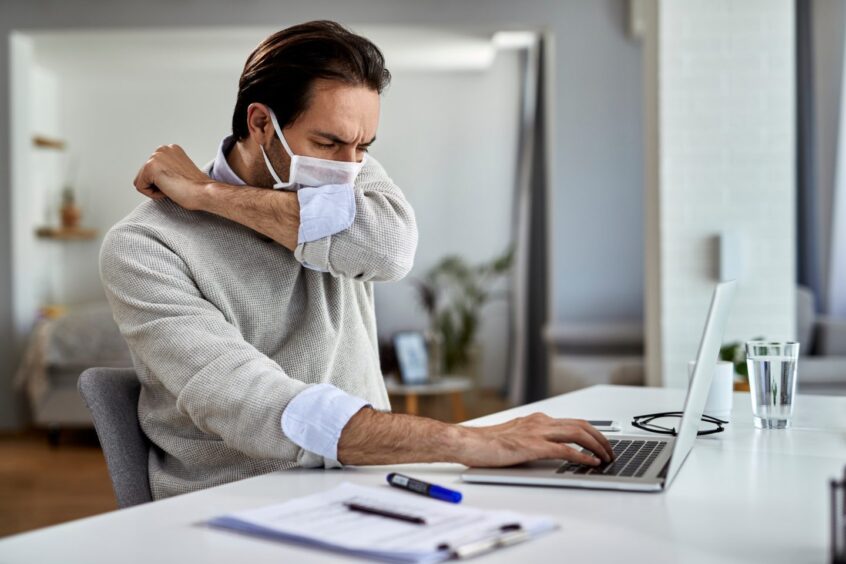 man coughs into his elbow while working on a laptop