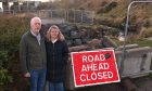 Garry and Anne Barclay standing beside a "Road Ahead Closed" sign.