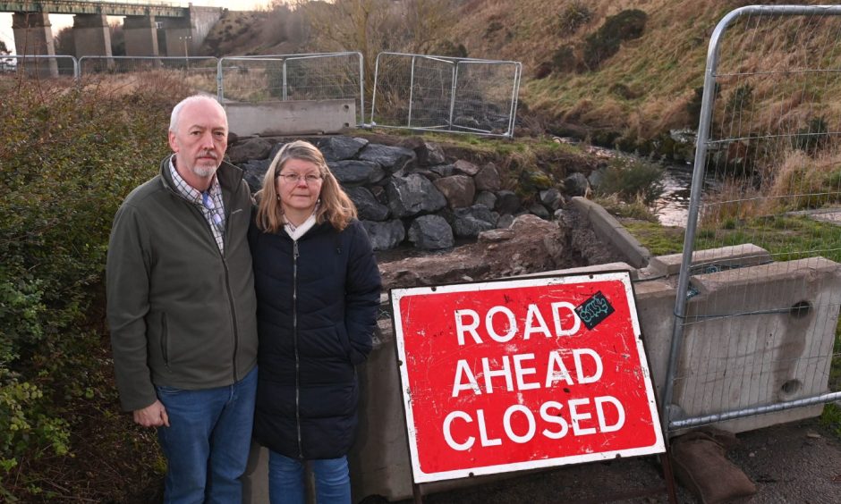 Garry and Annie Barclay standing beside a "Road Ahead Closed" sign.