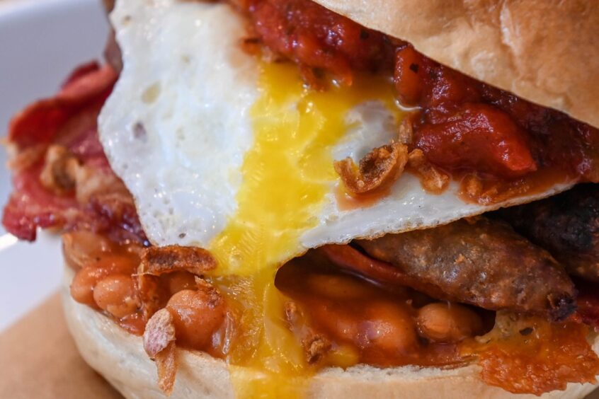 Close up of filled bagel bun featuring egg, beans and bacon.