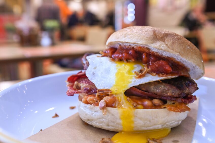 A filled breakfast bagel with fried egg, sausage, bacon and beens