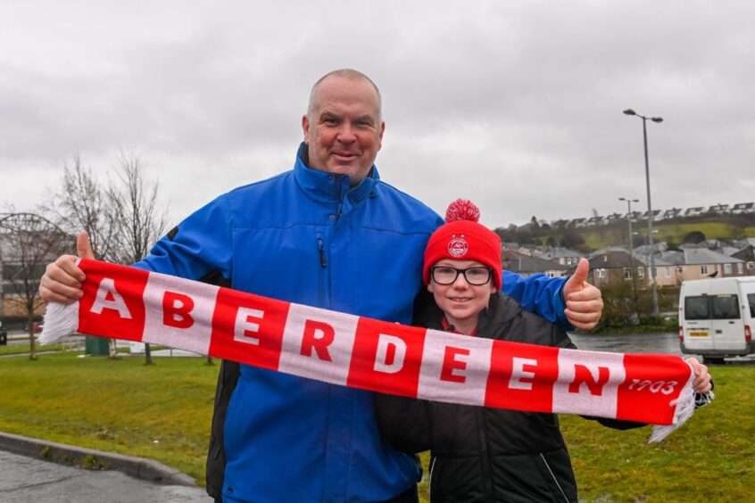 Man and child pose with 'Aberdeen' sign ahead of Viaplay Cup final against Rangers at Hampden Park.