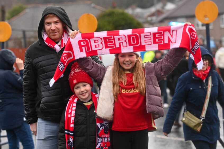 Young boy and girl smile while holding Aberdeen scarf ahead of game v Rangers.