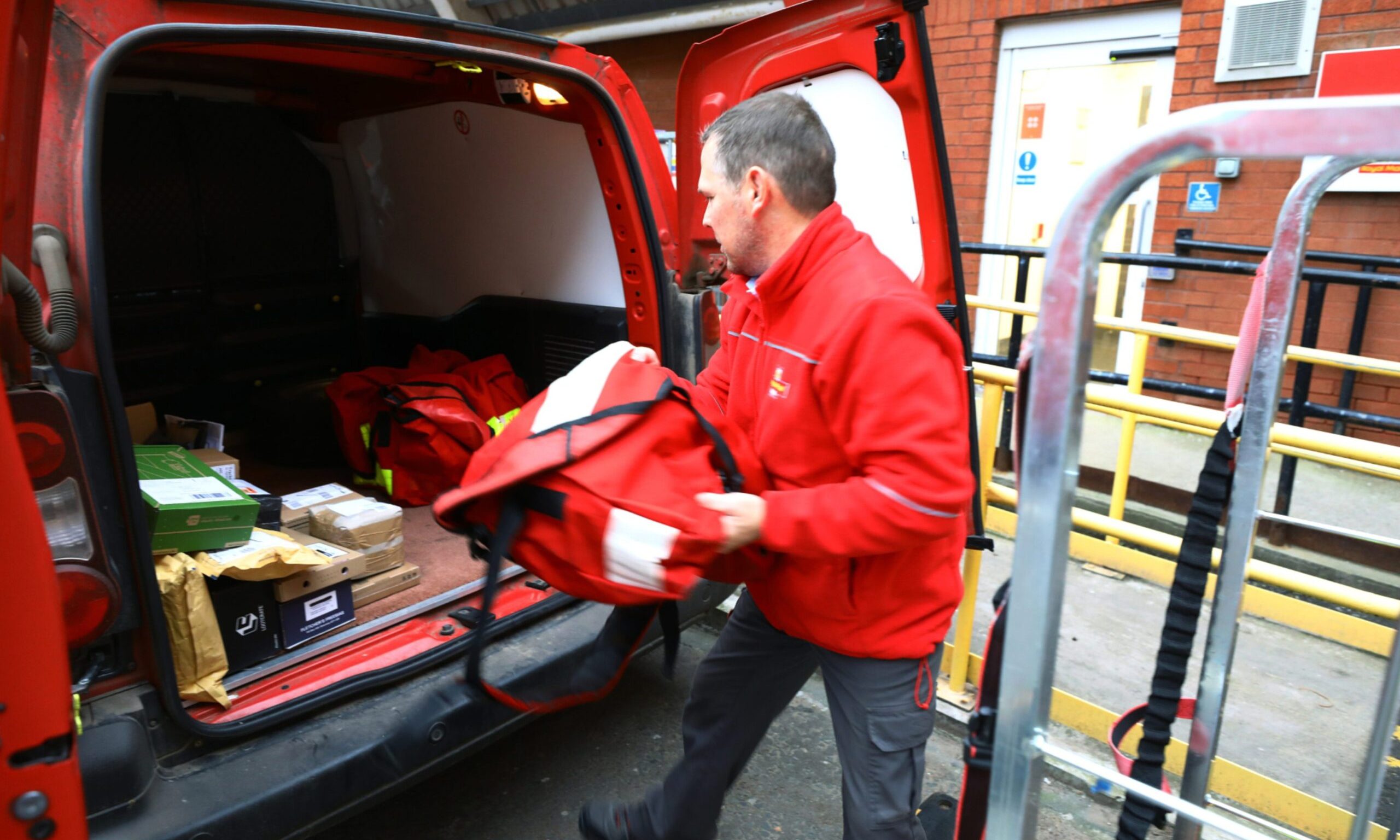 Royal Mail worker putting post in back of van. 
