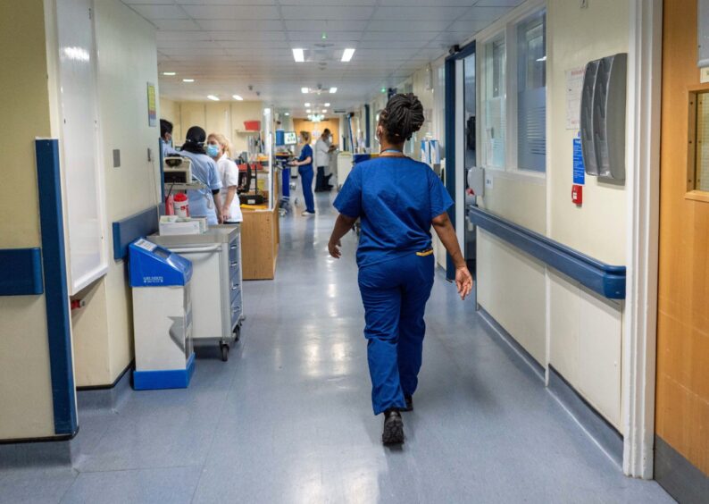 A nurse in blue scrubs walks through a busy hospital ward.