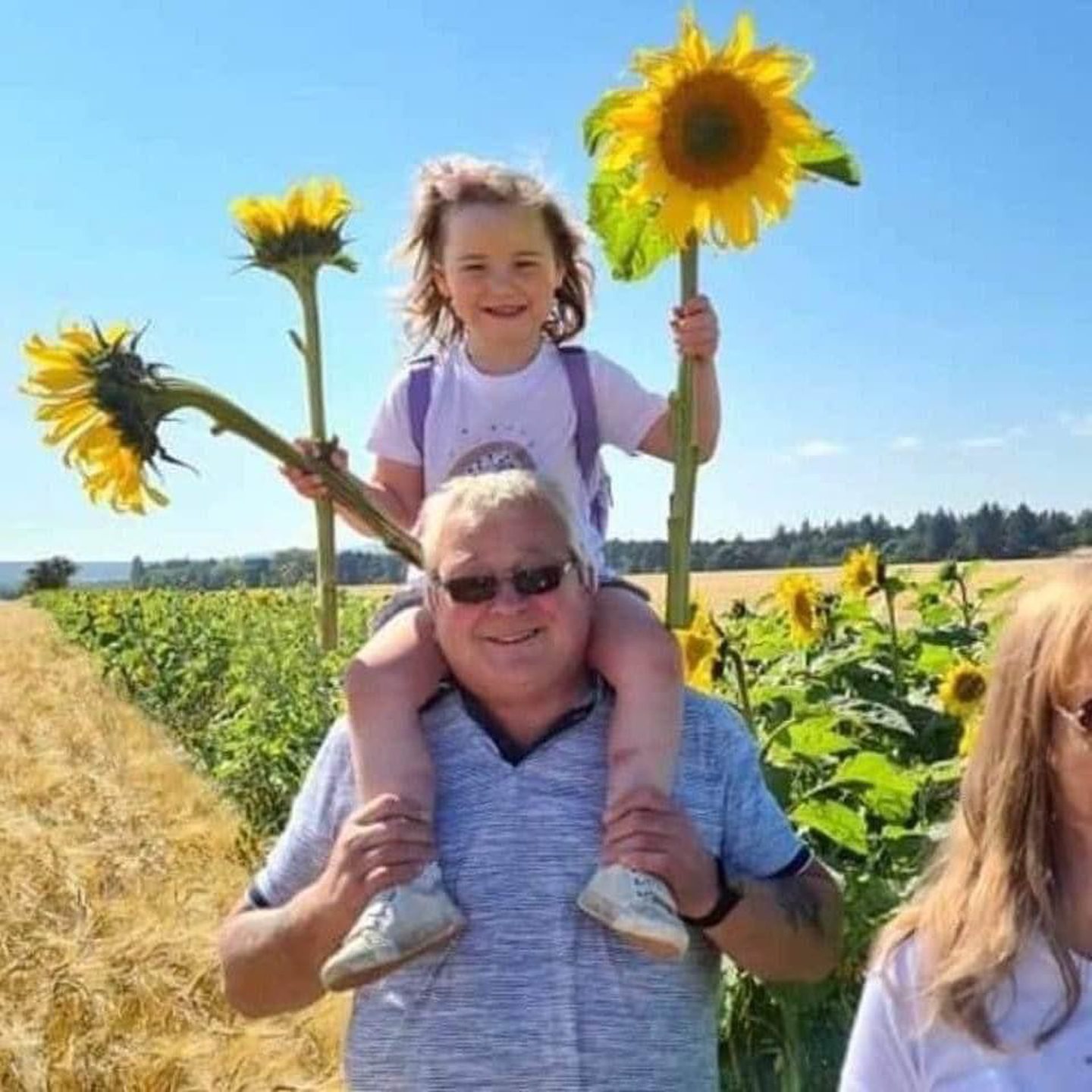 Tommy Neilson with a grandchild on his shoulders holding giant sunflowers