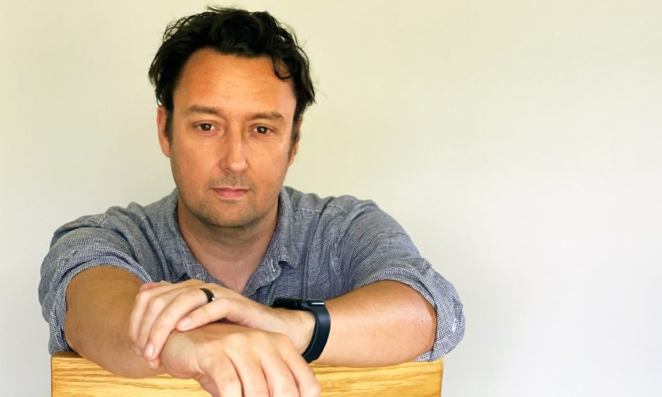 Author JD Kirk sitting on a chair and looking at the camera.