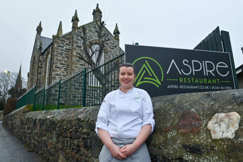 Jill Christine Mair standing outside the Aspire sign and restaurant inside church in Portsoy. 